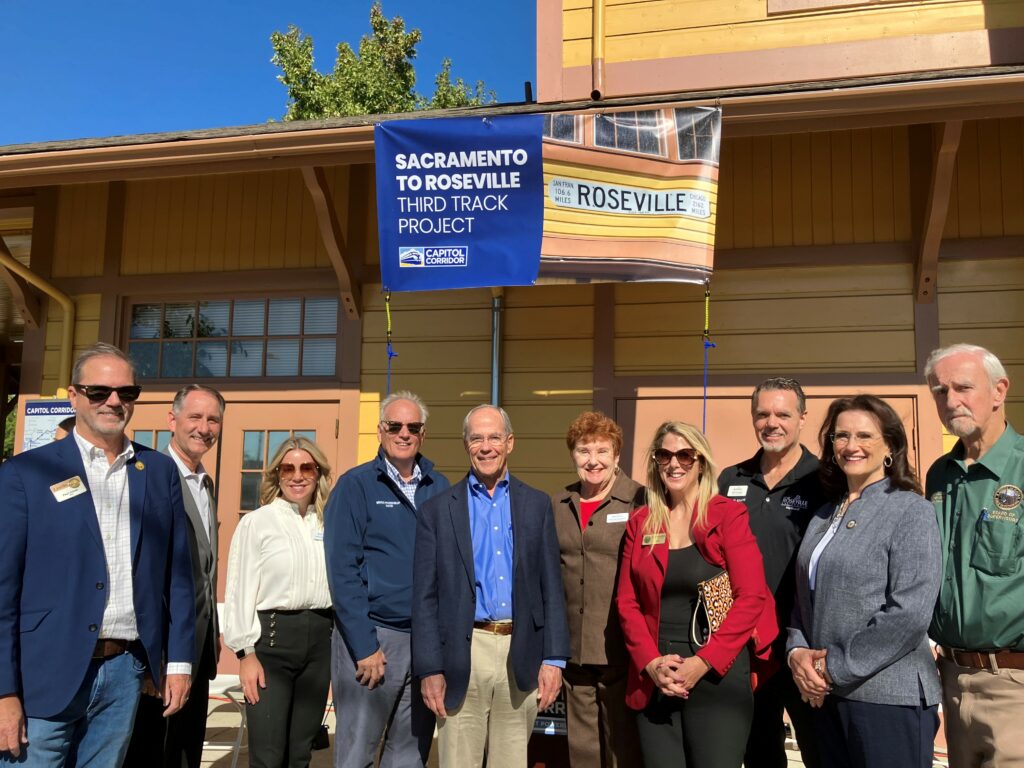 Elected officials posing for a photo in front of a train station